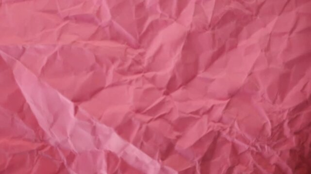Close-up full frame view of bright pink crumpled paper texture. Detailed background showing creases and wrinkles, suitable for craft, graphic design, text overlay, or stop motion animation concepts.