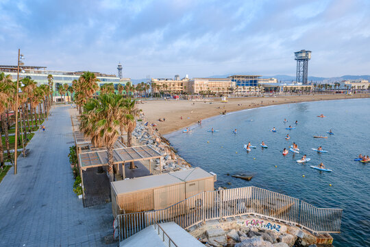 Sant Sebastia Beach Aerial View with Paddle Boarders in Barcelona, Promenade Palm Trees, Cable Car Tower, Morning Coastline