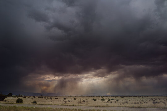 View of smoke from a wildfire rising over the dry plains under dark, dramatic storm clouds in CO, United States.