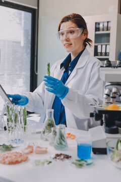 Scientists in lab coats work with plants in a modern lab, focusing on research and experimentation under bright, sterile conditions.