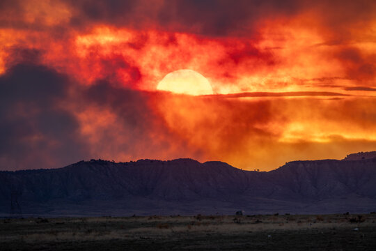 View of a dramatic sunset with the sun partially obscured by fiery red and orange clouds over a mountain range in Colorado Springs, CO, United States.