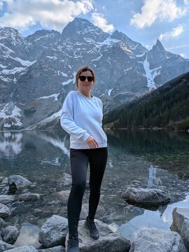Young woman hiker standing on rocks by scenic alpine mountain lake Morskie Oko in Tatra National Park during summer trek, active lifestyle, travel exploration, wellness and outdoor adventure vacation
