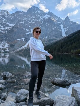 Young woman hiker standing on rocks by scenic alpine mountain lake Morskie Oko in Tatra National Park during summer trek, active lifestyle, travel exploration, wellness and outdoor adventure vacation