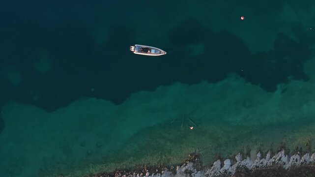 Aerial view of a small boat floating in the clear turquoise waters near the rocky coastline of Porto Palermo, Qarku i Vlores, Albania.