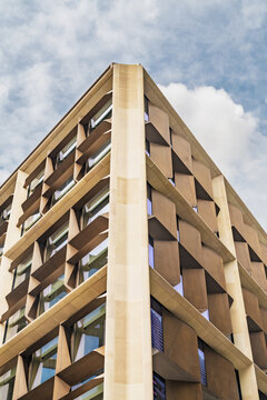 View of the modern architectural facade of a building in the City of London featuring geometric bronze sunshades and stone structural elements against a blue sky, London, England, United Kingdom.