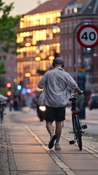 Young man walking with his bicycle on a city sidewalk during golden hour.
