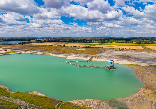 A green lake with a large machine on the shore and fields around. A green lake with a large machine on the shore and fields around. The sky has many clouds.