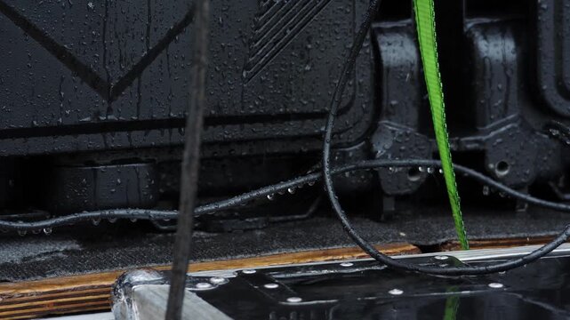 Close-up of wet black electrical panel with green cable under rain. Water droplets on exposed contacts create severe short circuit hazard, potential fire, dangerous outdoor safety risk. 4k video