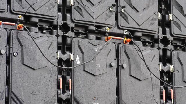 Multiple interconnected black electrical junction panels with power connectors and cables under heavy rain. Water droplets create critical short circuit hazard, fire danger, electrocution, risk 4k
