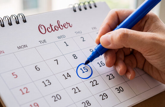 Hand Circling 15th of October Date on Desk Calendar with Blue Marker