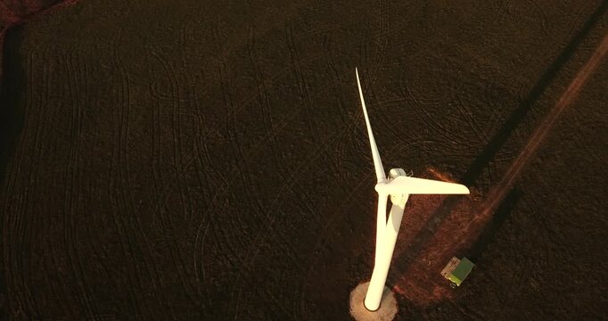 Aerial view of a single wind turbine standing in a dark, plowed field during golden hour in Devon, England, United Kingdom.