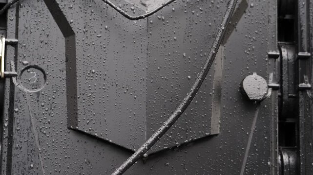 Wet black electrical housing panel covered in raindrops. Outdoor industrial equipment under heavy rain creates severe short circuit fire safety hazard possible electrocution 4k shot