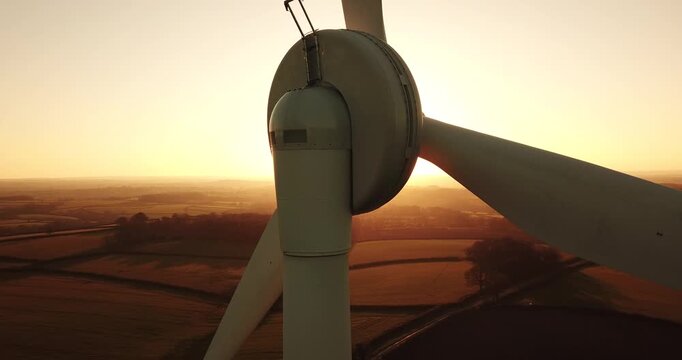 Aerial view of a wind turbine at sunset with golden light over the rural landscape of Devon, England, United Kingdom.