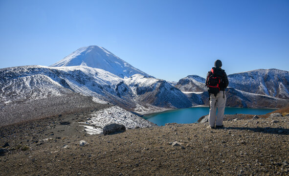 Hiker admiring Upper Tama Lake and snow-capped Mount Ngauruhoe. Tama Lakes Track. Tongariro National Park. New Zealand.