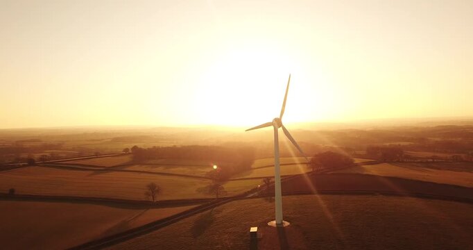 Aerial view of a wind turbine standing in a rural field during a golden sunset in Devon, England, United Kingdom.