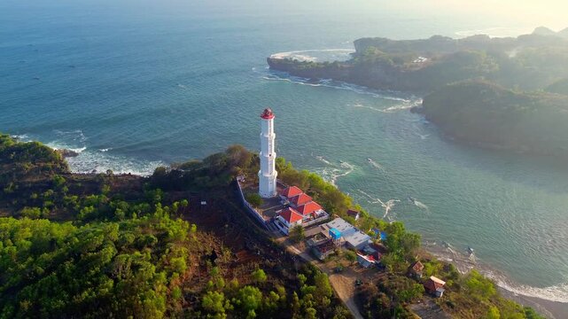 Aerial view of Baron Lighthouse on a coastal cliff overlooking the Indian Ocean with lush vegetation and waves in Yogyakarta, Special Region of Yogyakarta, Indonesia.
