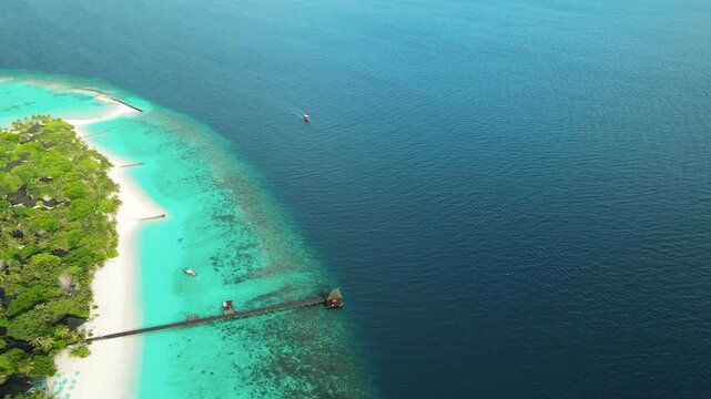 Aerial view of Meedhupparu island with turquoise lagoon and wooden jetty in Raa Atoll, Maldives.