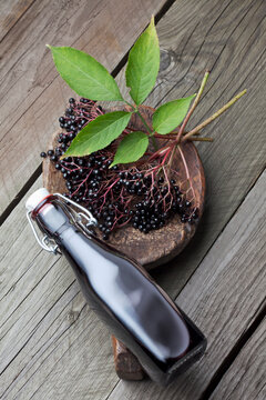 Elderberries (Sambucus), leaves on a wooden shovel and a bottle of elderberry juice on white wooden table, studio shot