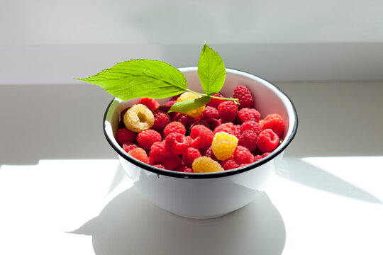 Bowl of red and yellow raspberries on window sill