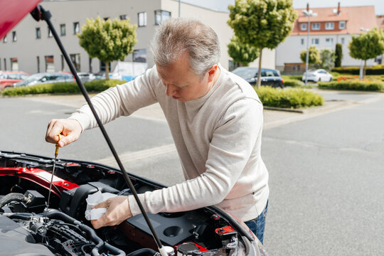 Driver checking car engine oil with dipstick outdoors