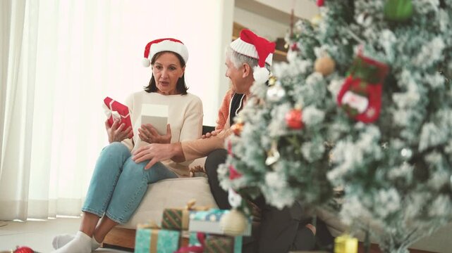 Elderly woman receiving Christmas gift from senior man while daughter shares the moment, holiday surprise, family bonding, gift giving, Christmas family celebration.