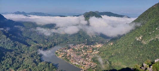 A breathtaking view of a serene mountain village surrounded by lush greenery and drifting clouds, capturing nature's beauty. © Vangly