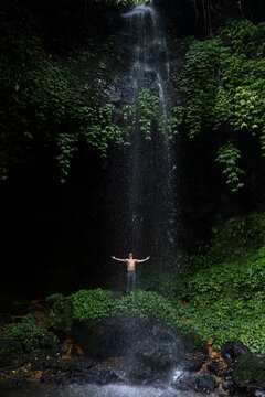 Man standing with arms outstretched at waterfall in Bali jungle