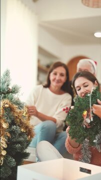 Three generation family decorating Christmas tree together at home, senior parents and adult daughter, Christmas preparation, holiday tradition, family relationship, festive season.