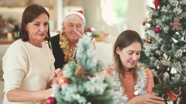 Adult daughter helping elderly parents decorate Christmas tree, multigenerational family, holiday celebration, Christmas ornaments, family bonding, festive home activity.