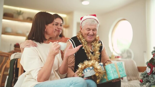 Senior man giving Christmas gift to senior woman while adult daughter hugs her parents, family celebration, Christmas surprise, holiday gift, multigenerational family.