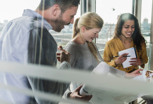 Three smiling colleagues looking at plan in office