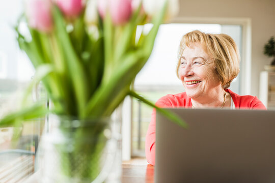 Smiling senior woman sitting at table with laptop