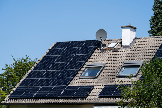 A house roof features modern solar panels under a clear blue sky