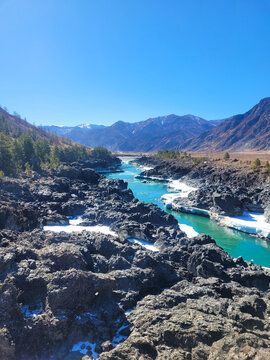 Altai, Russia, Turquoise mountain river flowing through rugged rocky gorge with patches of white snow under a clear sky