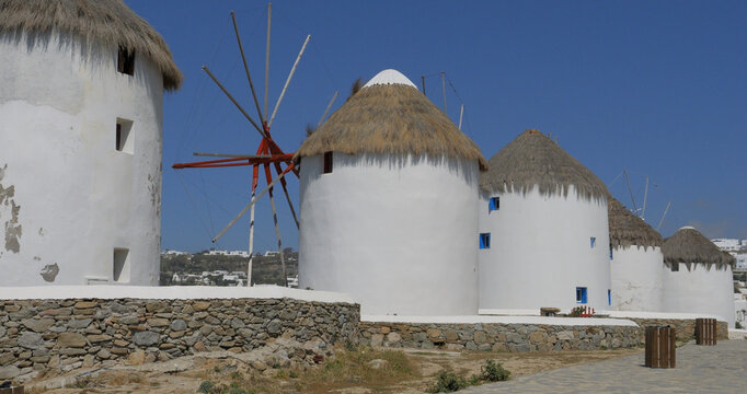 View of the iconic white windmills of Mykonos with thatched roofs and stone walls under a clear blue sky in Mykonos, Greece.