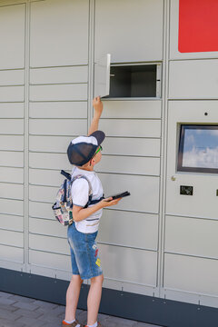 Young boy closing an empty compartment of an automated parcel locker after collecting an online order. Concept of self service, contactless delivery and independent parcel collection.