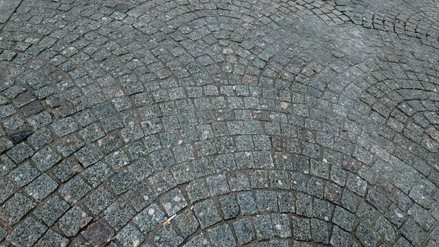 Curved cobblestone pavement texture with natural stone pattern, gray paving surface background for architectural design, urban landscape and vintage street concepts