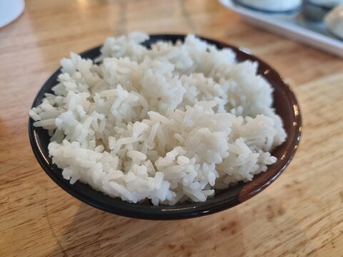 Steaming Bowl of Rice: A close-up shot of a rustic bowl overflowing with perfectly cooked, fluffy white rice, ready to be served as a comforting meal.