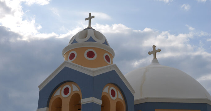 View of the iconic blue and orange domed church with crosses against a cloudy sky in Fira, Greece.