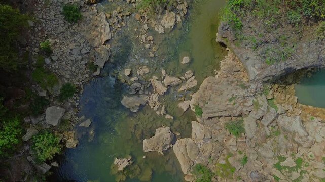 Aerial view of Sri Gethuk Waterfall with rocky riverbed, lush greenery, and flowing water in Yogyakarta, Special Region of Yogyakarta, Indonesia.