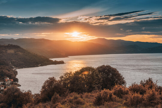 Warm golden sunset bathes a wide river gorge and forested hillside village in glowing autumn light, evoking peace and wanderlust.