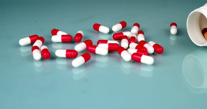 Smooth horizontal camera pan gliding over scattered white and red medicine capsules to reveal a white plastic drug bottle on a light blue glass tabletop, clinical healthcare and pharmacy layout