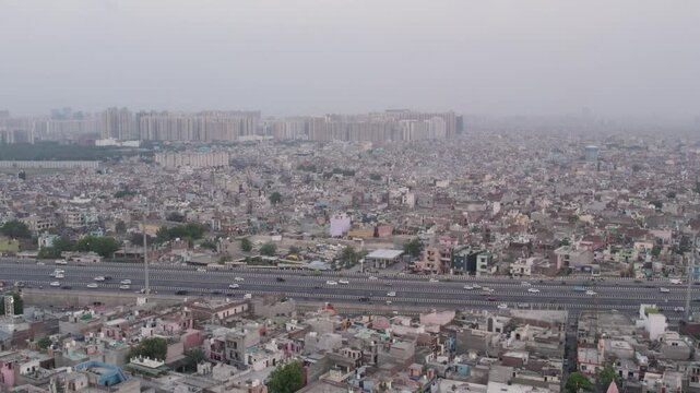 Aerial view of the dense urban landscape with a busy highway cutting through the city, surrounded by residential buildings and distant high-rise apartments in Ghaziabad, Uttar Pradesh, India.