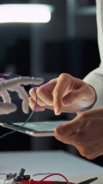 Lab-coated researcher manipulates tablet while assembling a robotic hand in a science laboratory, using precision tools to advance robotics technology and ongoing research, under controlled lighting