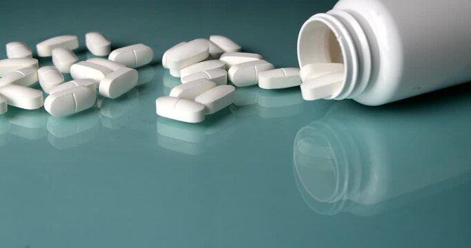 Horizontal camera slider motion tracking along white pharmaceutical tablets towards an upright white bottle on a light blue glass surface, medical treatment and prescription setup
