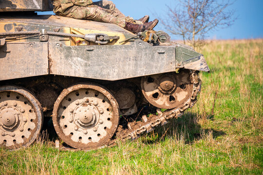 View of British Army armoured vehicle tracks on the muddy terrain of Salisbury Plain with a soldier sitting on the hull in Salisbury, Wilshire, United Kingdom.