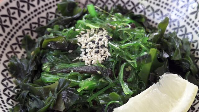 Fresh hiyashi wakame seaweed salad with sesame seeds and lemon served in a patterned bowl.