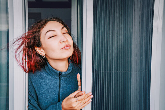 Smiling woman looking through a mosquito screen door onto a sunny balcony, enjoying fresh air and protection from insects during summer