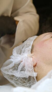 Professional beautician applying cleansing mask on female client's face. Close-up of female face during youth restoration and facial rejuvenation procedure  - Vertical Video