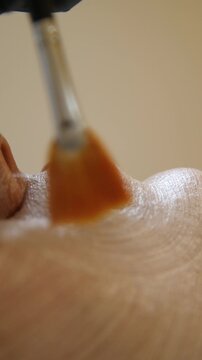 Professional beautician applying cleansing mask on female client's face. Close-up of female face during youth restoration and facial rejuvenation procedure  - Vertical Video